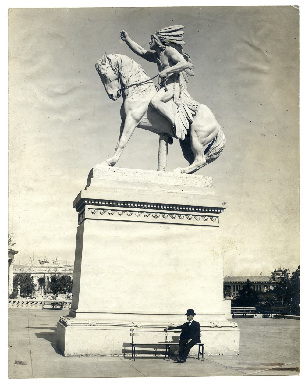 Fotografia verticale in seppia che mostra una statua di un indiano americano seduto su un cavallo sopra un grande piedistallo. C