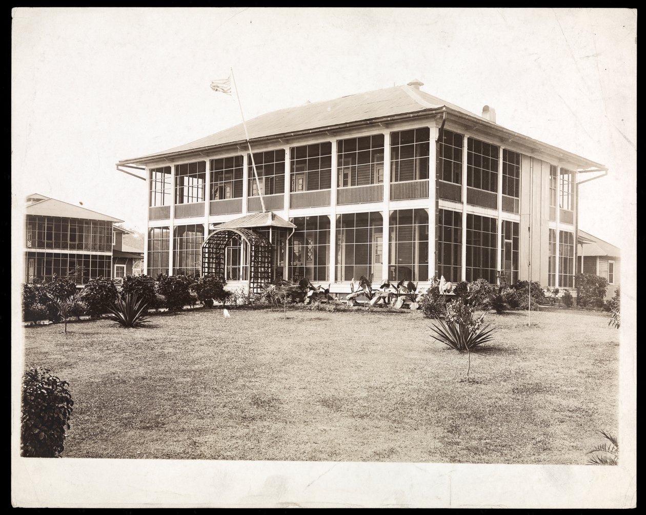 Una casa a due piani circondata da portici, con una bandiera americana che sventola; a Panama durante la costruzione del canale, 1912 da Byron Company