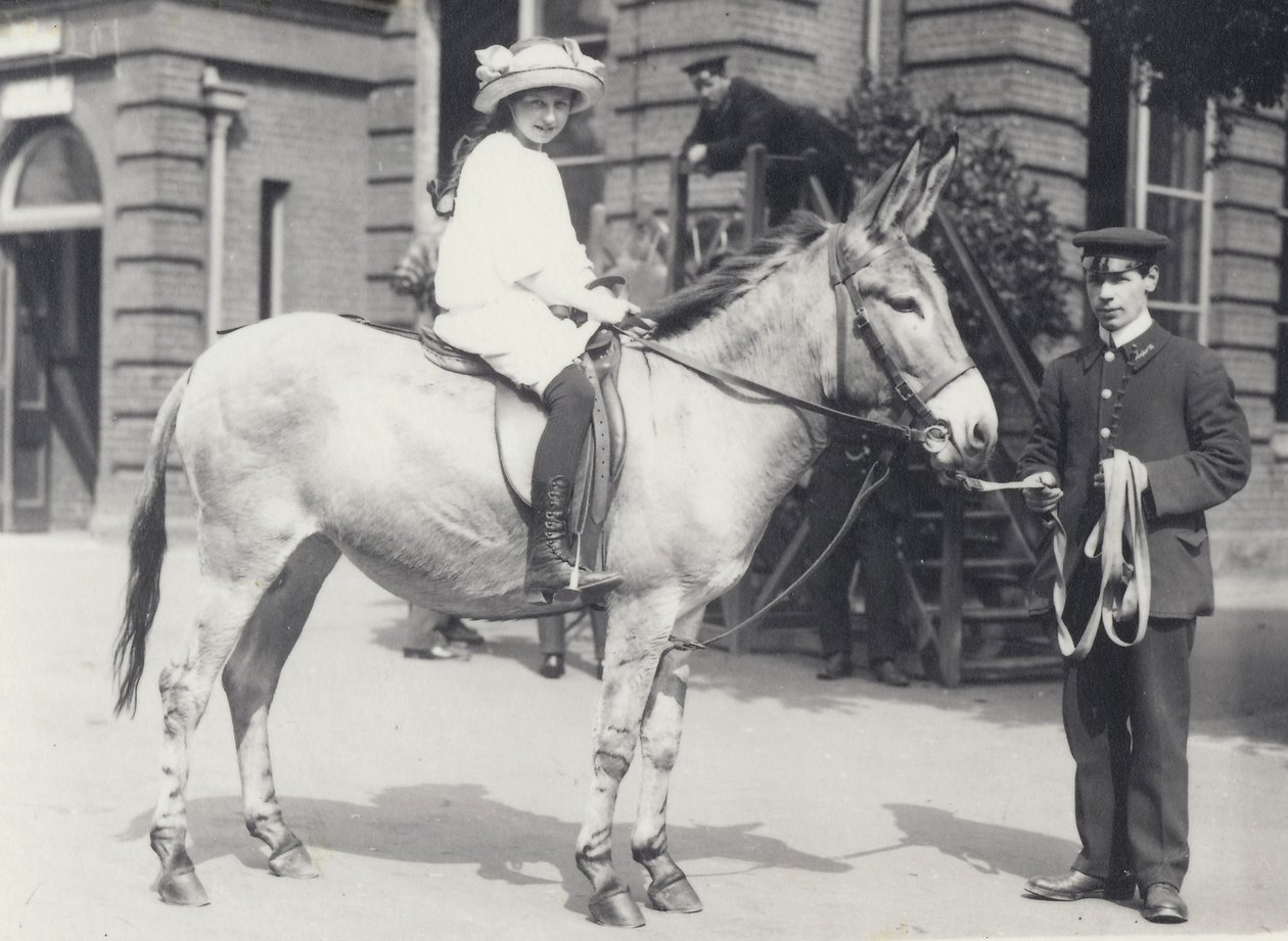 Una giovane donna cavalca un asino guidato da un custode mentre un altro osserva, Zoo di Londra, maggio 1914 da Frederick William Bond