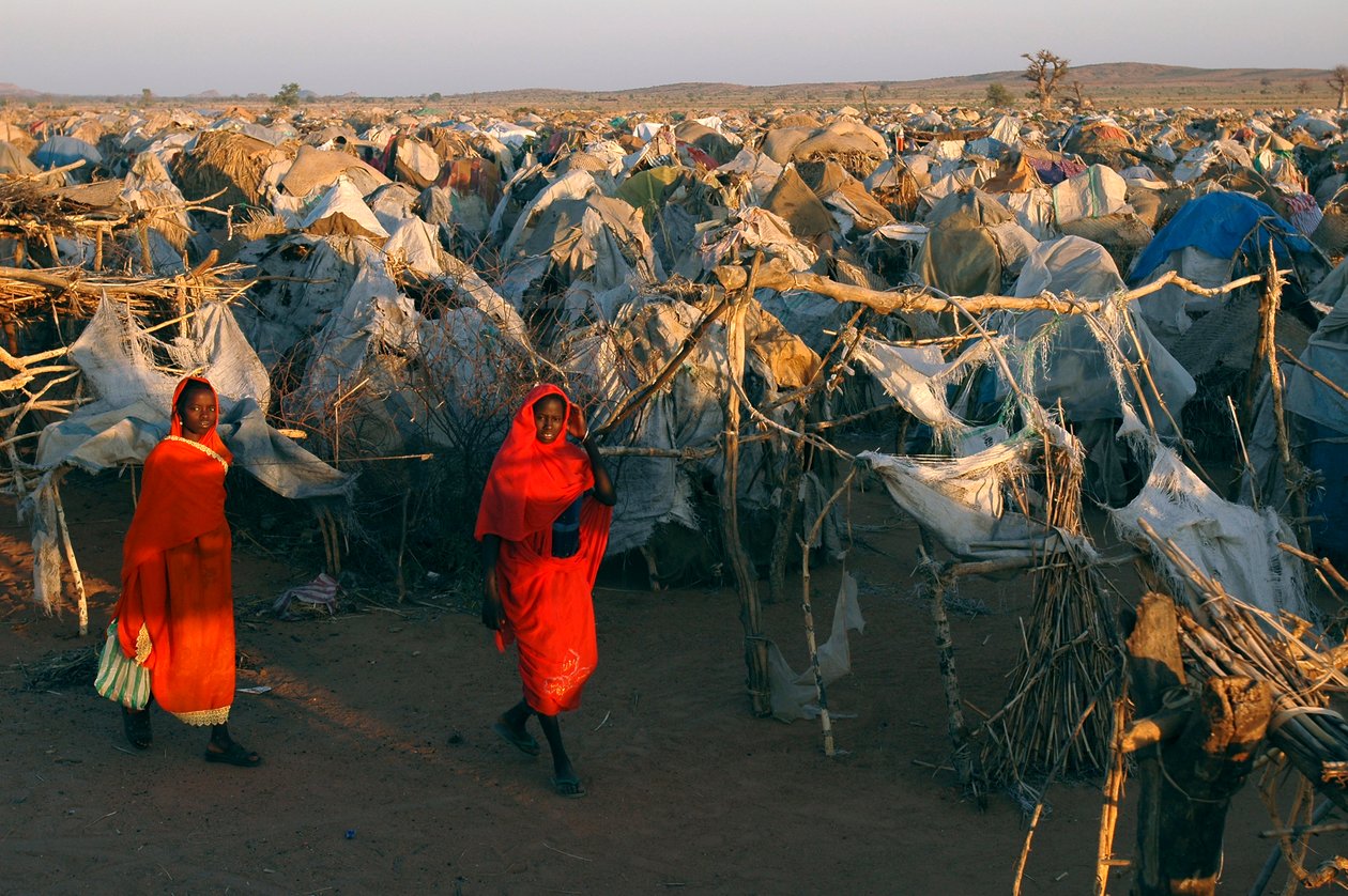 Vestite di rosso vivo, le donne camminano attraverso il campo di Otash per Persone Sfollate Internamente da Unbekannt Unbekannt