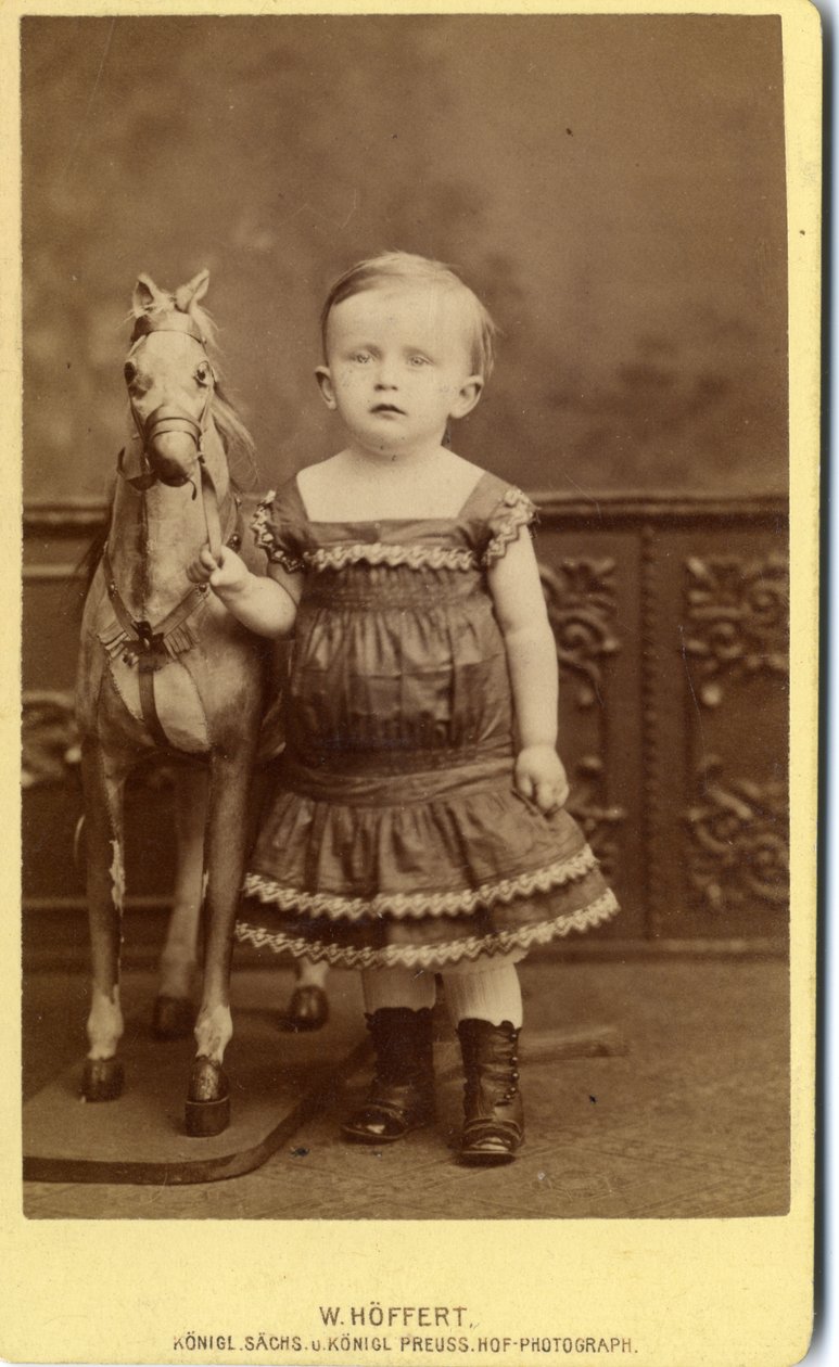 Bambina in piedi accanto a un cavallo a dondolo da W. Hoffert